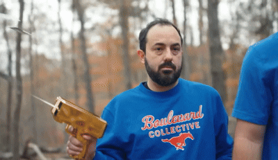 a man wearing a blue boulevard collective sweatshirt is holding a gun