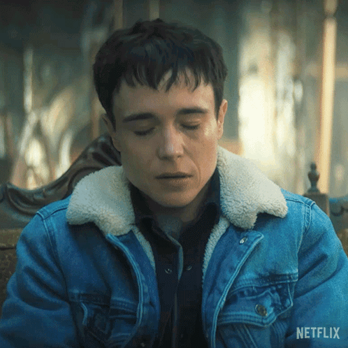 A Man Wearing A Blue Denim Jacket With A Sherpa Collar Is Sitting On A Chair With His Eyes Closed . GIF