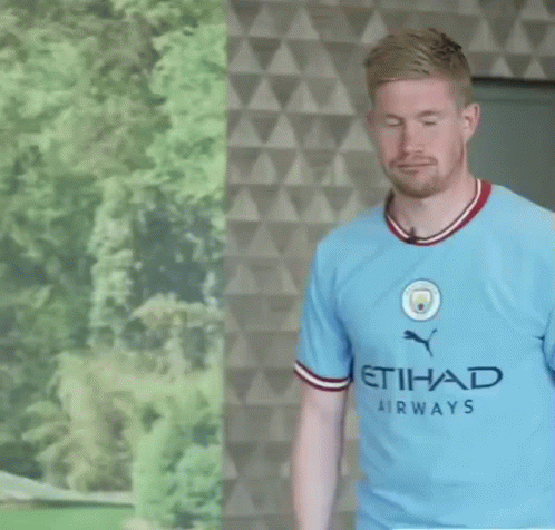 A Man Wearing A Blue Etihad Airways Shirt Stands In Front Of A Wall GIF