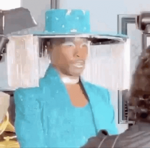 A Man Wearing A Blue Hat And A Blue Jacket Is Standing In Front Of A Camera . GIF