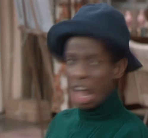 A Man Wearing A Blue Hat And A Green Turtleneck Sweater Is Making A Funny Face . GIF