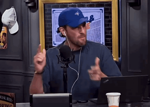 A Man Wearing A Blue Hat And Ear Buds Talking Into A Microphone GIF