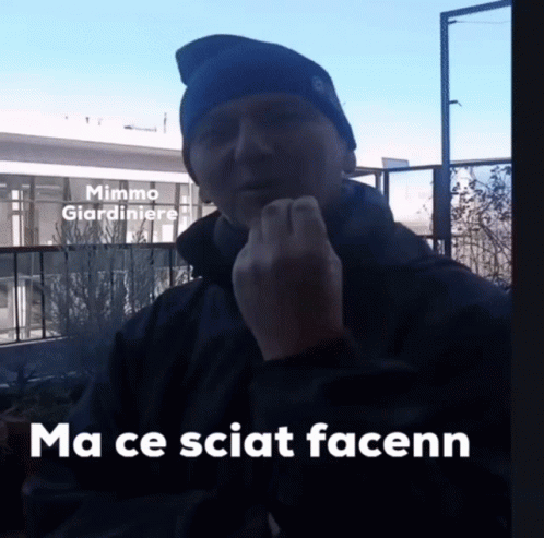 A Man Wearing A Blue Hat Is Giving The Middle Finger In Front Of A Building That Says Mimmo Giardiniere On It GIF