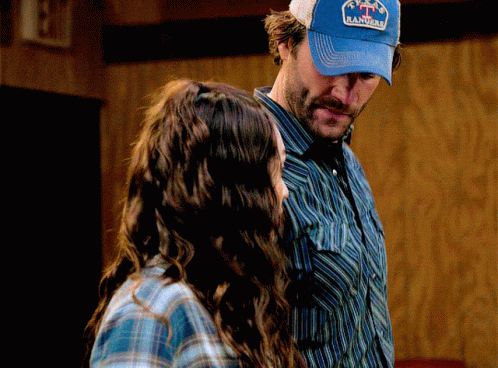 A Man Wearing A Blue Hat That Says Rancho Stands Next To A Woman GIF