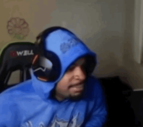 A Man Wearing A Blue Hoodie And Headphones Is Sitting In A Chair In Front Of A Computer . GIF