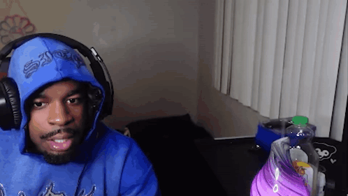 A Man Wearing A Blue Hoodie And Headphones Is Sitting In Front Of A Computer . GIF