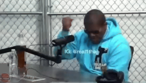 A Man Wearing A Blue Hoodie Is Sitting In Front Of A Microphone . GIF