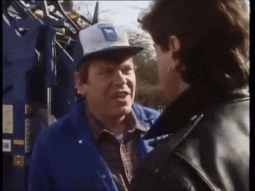 a man wearing a blue jacket and a white hat with the letter m on it talks to another man