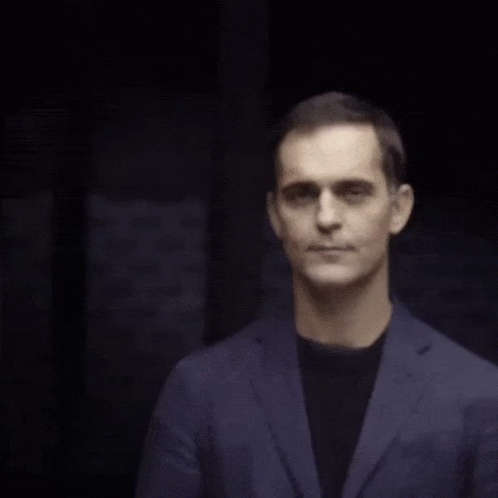 A Man Wearing A Blue Jacket And Black Shirt Is Smiling GIF
