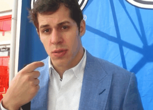 A Man Wearing A Blue Jacket And White Shirt Is Pointing At Something GIF