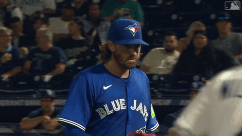 A Man Wearing A Blue Jays Jersey Stands In A Crowd GIF