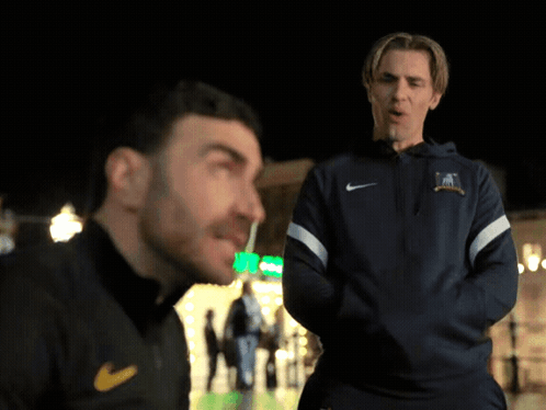 A Man Wearing A Blue Nike Jacket Talks To Another Man GIF