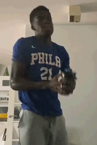 A Man Wearing A Blue Philadelphia Shirt Is Holding A Bottle GIF
