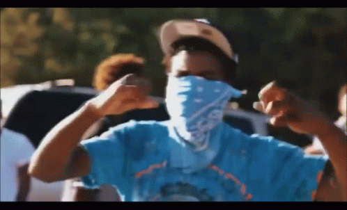 A Man Wearing A Blue Shirt And A Bandana On His Face Is Making A Fist . GIF