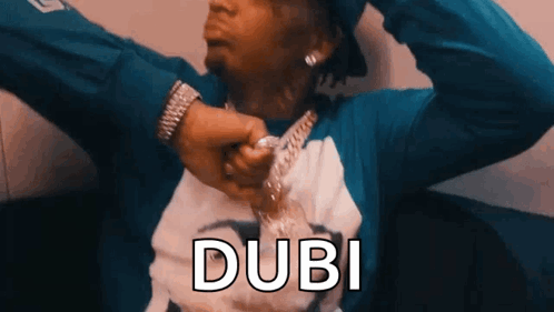 A Man Wearing A Blue Shirt And A Watch Is Holding A Chain Around His Neck And The Word Dubi Is Above Him . GIF