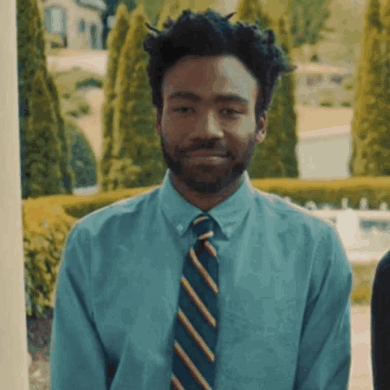 A Man Wearing A Blue Shirt And Striped Tie Smiles GIF