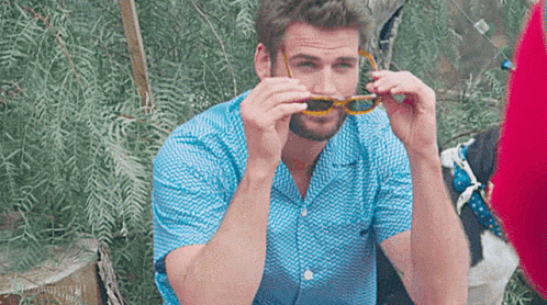 A Man Wearing A Blue Shirt And Sunglasses Is Sitting On A Chair . GIF