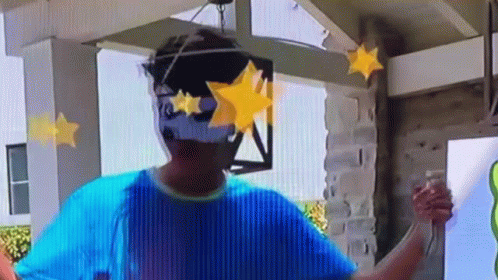 A Man Wearing A Blue Shirt And Sunglasses Is Standing In Front Of A Building With Stars On His Face . GIF