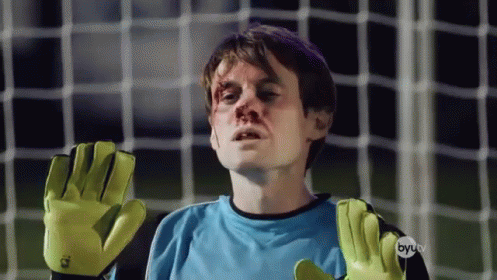 A Man Wearing A Blue Shirt And Yellow Gloves Stands In Front Of A Soccer Net GIF