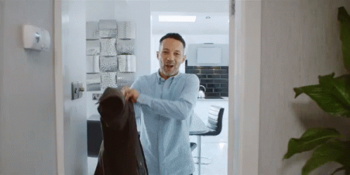 A Man Wearing A Blue Shirt Is Holding A Black Jacket GIF