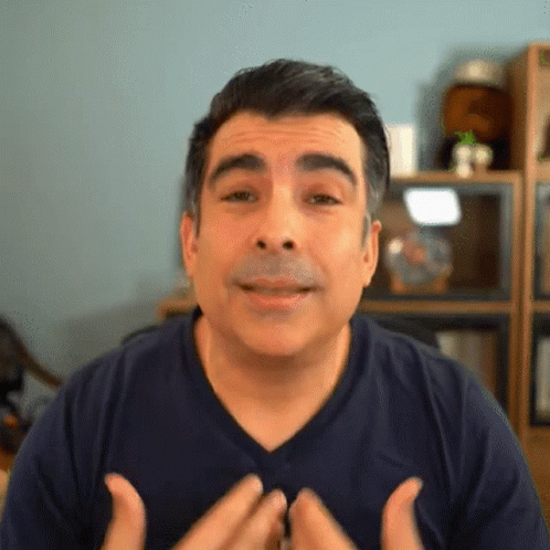 A Man Wearing A Blue Shirt Is Making A Face With His Hands GIF