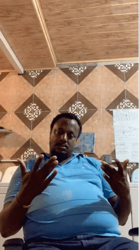 A Man Wearing A Blue Shirt Is Sitting In Front Of A Wall With A Calendar On It GIF