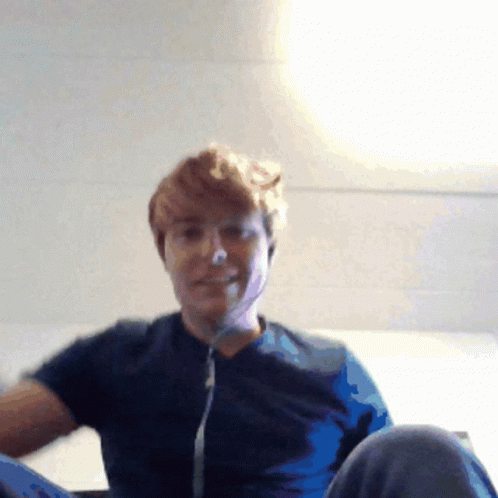 A Man Wearing A Blue Shirt Is Sitting On A Bed GIF