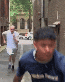 A Man Wearing A Blue Shirt That Says ' Washington ' On It Is Running Down A Street GIF