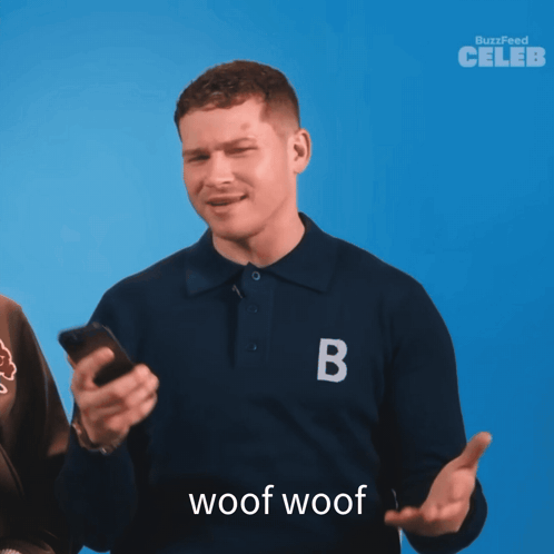 A Man Wearing A Blue Shirt With The Letter B On It Holds A Cell Phone GIF