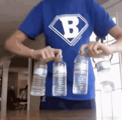 A Man Wearing A Blue Shirt With The Letter B On It Is Holding Two Water Bottles . GIF