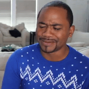 A Man Wearing A Blue Sweater Is Making A Funny Face In A Living Room . GIF
