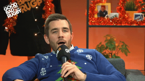 A Man Wearing A Blue Sweater Is Talking Into A Microphone With The Words Good Bad And Rugby Written In The Background GIF