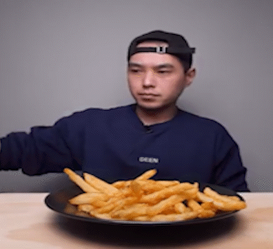 a man wearing a blue sweater that says seen is eating french fries