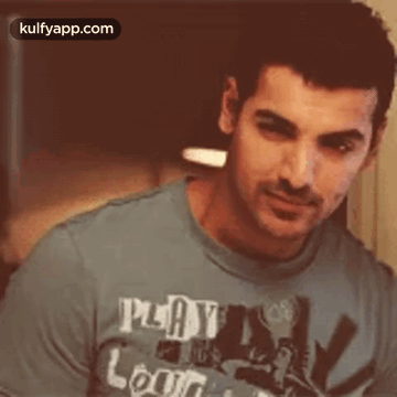 A Man Wearing A Blue T-Shirt That Says `` Play And Learn '' Is Looking At The Camera . GIF