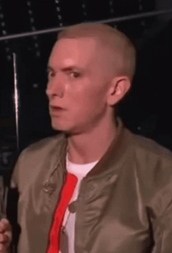 A Man Wearing A Bomber Jacket And A Red Tie Is Talking Into A Microphone GIF