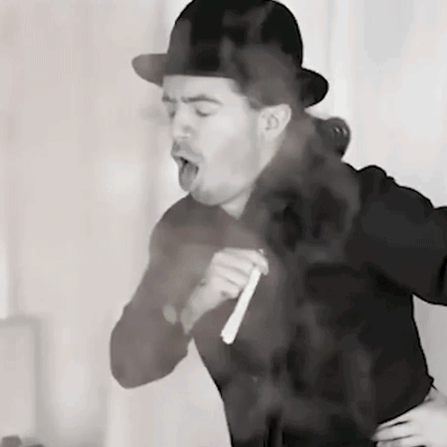 A Man Wearing A Bowler Hat Is Smoking A Cigarette In A Black And White Photo GIF