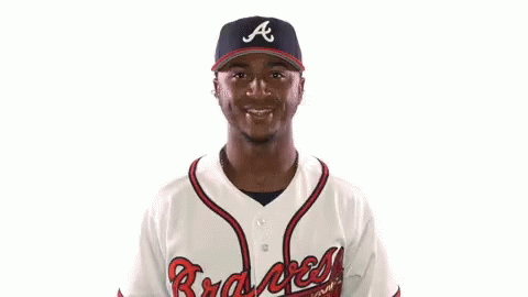 A Man Wearing A Braves Jersey Holds His Arms Up In The Air GIF