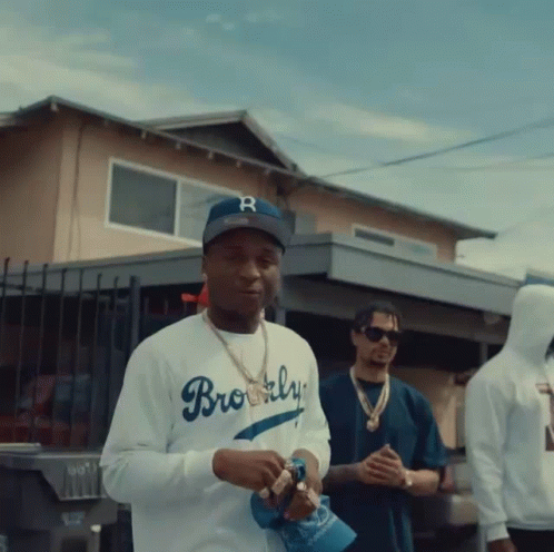 a man wearing a brooklyn baseball cap stands in front of a house
