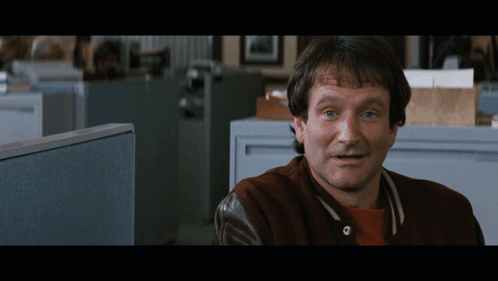 A Man Wearing A Brown Jacket Is Sitting In An Office Cubicle GIF