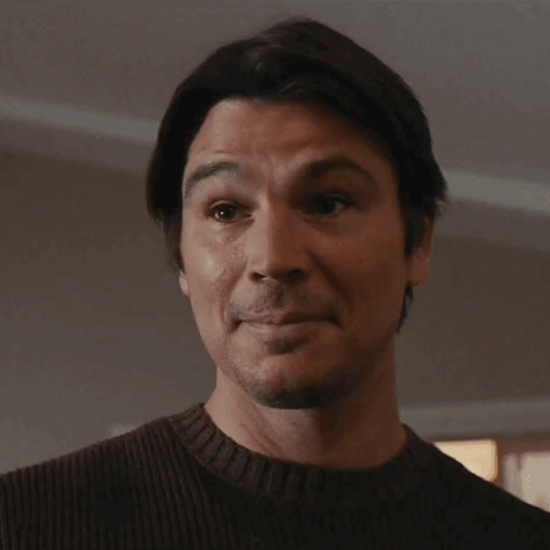 A Man Wearing A Brown Sweater Is Looking At The Camera GIF
