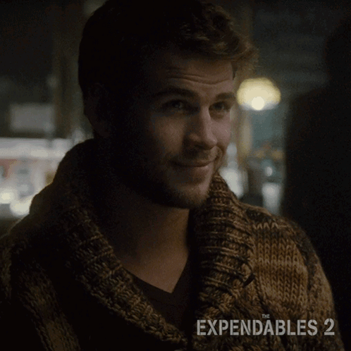 A Man Wearing A Brown Sweater With The Expendables 2 On The Bottom GIF