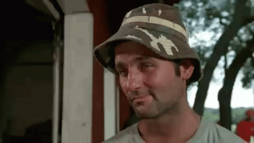 A Man Wearing A Bucket Hat Is Making A Funny Face And Smiling . GIF