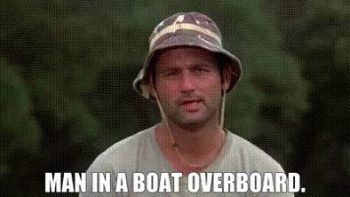 A Man Wearing A Bucket Hat Is Standing In Front Of A Green Background And Says `` Man In A Boat Overboard . '' GIF