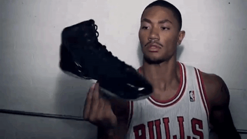 A Man Wearing A Bulls Jersey Holds Up A Black Shoe GIF