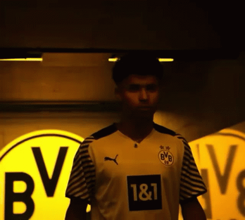 A Man Wearing A Bvb Jersey Stands In Front Of A Yellow Sign GIF
