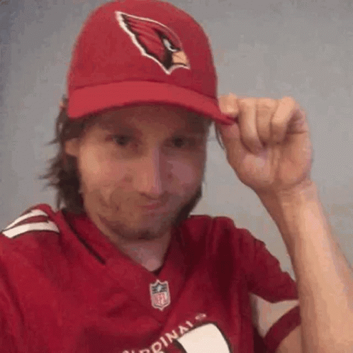 A Man Wearing A Cardinals Hat And A Red Jersey Is Adjusting His Hat . GIF
