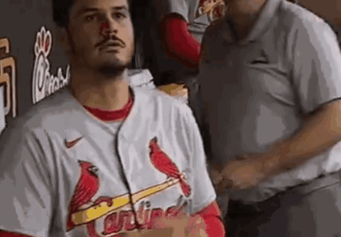 A Man Wearing A Cardinals Jersey Is Standing In A Dugout With A Red Nose . GIF