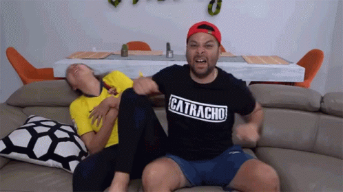 A Man Wearing A Catracha Shirt Sits On A Couch GIF