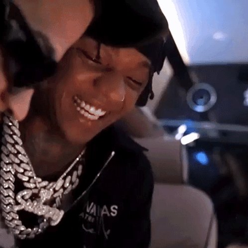 A Man Wearing A Chain Around His Neck Is Smiling While Another Man Looks On . GIF