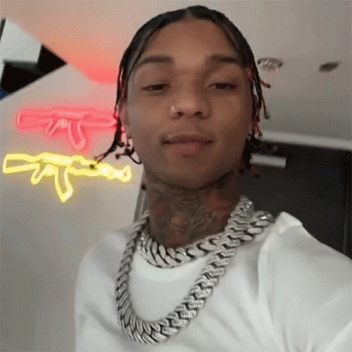 A Man Wearing A Chain Around His Neck Is Taking A Selfie In Front Of A Neon Sign . GIF
